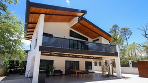 Ein modernes, zweistöckiges Haus mit Balkon, großen Fenstern und einer Terrassenfläche.