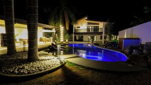 Ein modernes Haus mit Schwimmbad, Sitzgelegenheiten im Freien und einem gut beleuchteten Patio.