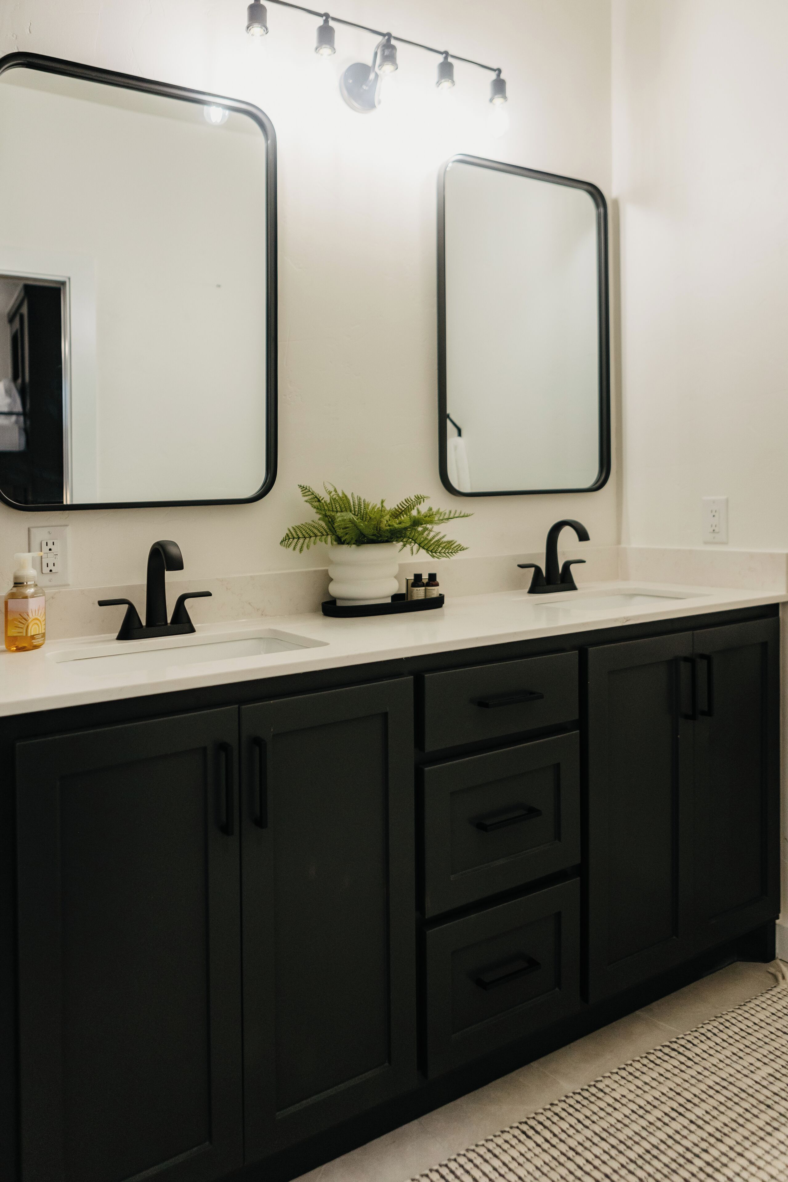 A bathroom with a white sink, black cabinets, and two mirrors.