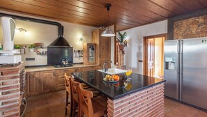 Cozinha com ilha central, armários de madeira, geladeira de aço inoxidável e parede decorada com tijolos.