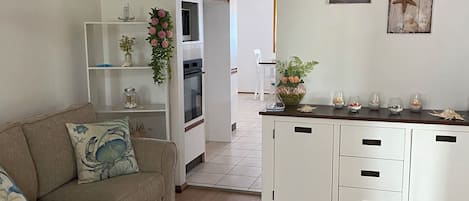 Een moderne keuken met witte kasten, een houten aanrechtblad en een inbouwoven. Er is een witte eethoek met een stoel en een kleine tafel. De kamer heeft houten vloeren en een plafondlamp.