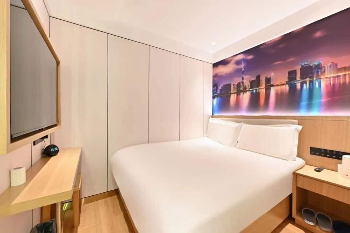 A modern hotel room with a large bed, a flat-screen TV, a desk, and a cityscape mural on the wall.