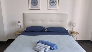 Una cama bien hecha con una colcha azul claro y almohadas, dos cuadros enmarcados en la pared y lámparas de noche a cada lado.