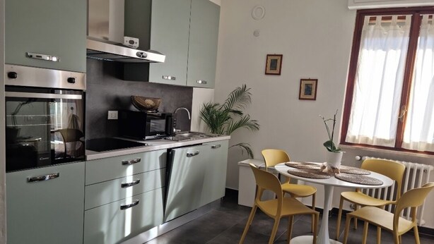 Una cocina moderna con horno empotrado, microondas y fregadero. Hay una mesa de comedor con cuatro sillas y una planta en maceta.