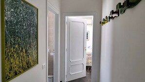 Un pasillo de diseño moderno, con un gran cuadro abstracto a la izquierda, una puerta blanca al final y una lámpara en el techo.