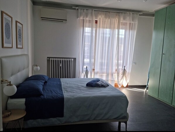 Un dormitorio con cama, radiador, ventana con cortinas y un armario verde.