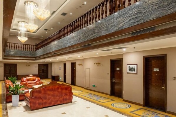 A hotel lobby with a central seating area, a marble staircase, and a high ceiling with chandeliers.
