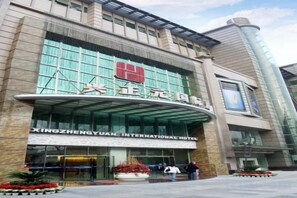 Een hotel met een grote glazen gevel, borden waarop Xingzhengyuan International Hotel staat vermeld, en een gebogen entree.