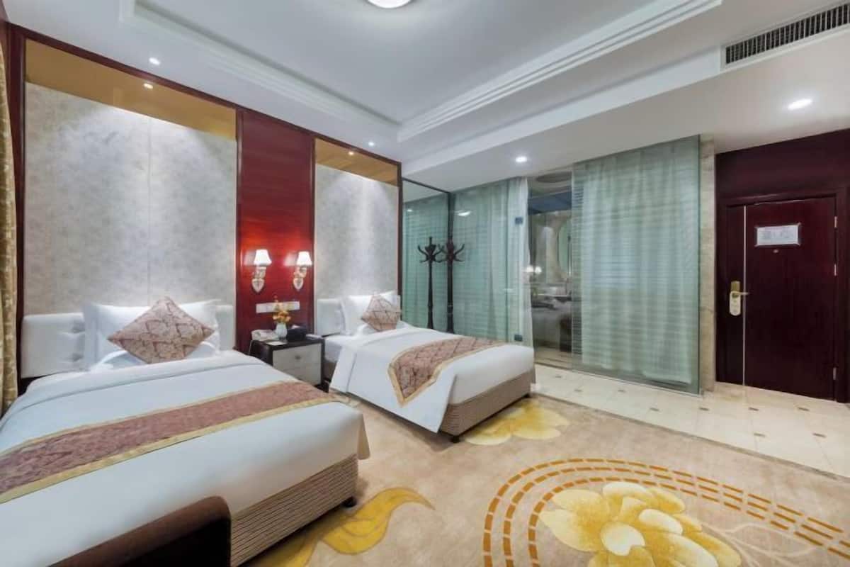 A hotel room with two beds, a large mirror, a nightstand, and a glass shower enclosure.
