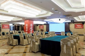 A conference room with rows of tables and chairs, a large screen, and a stage.