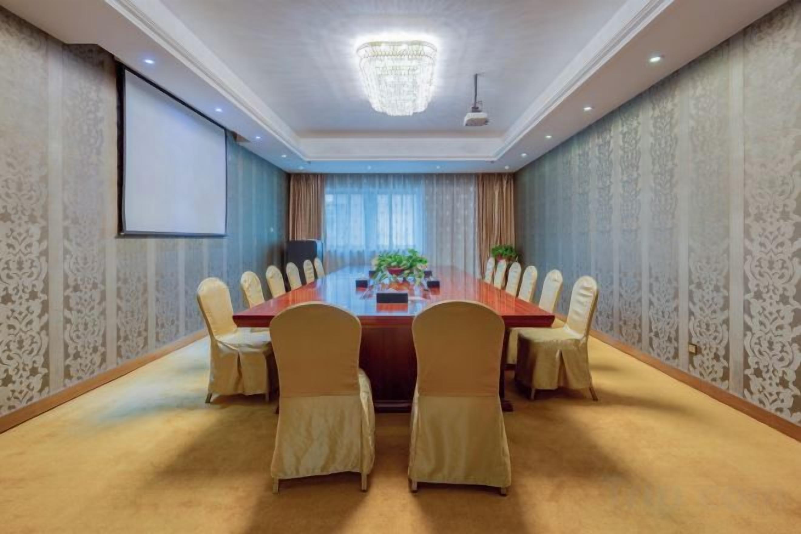 Une salle de conférence avec une longue table, des chaises, un écran de projection et un lustre.