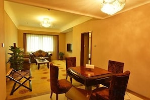 A hotel room with a dining area, a sofa, a TV, and a large window.