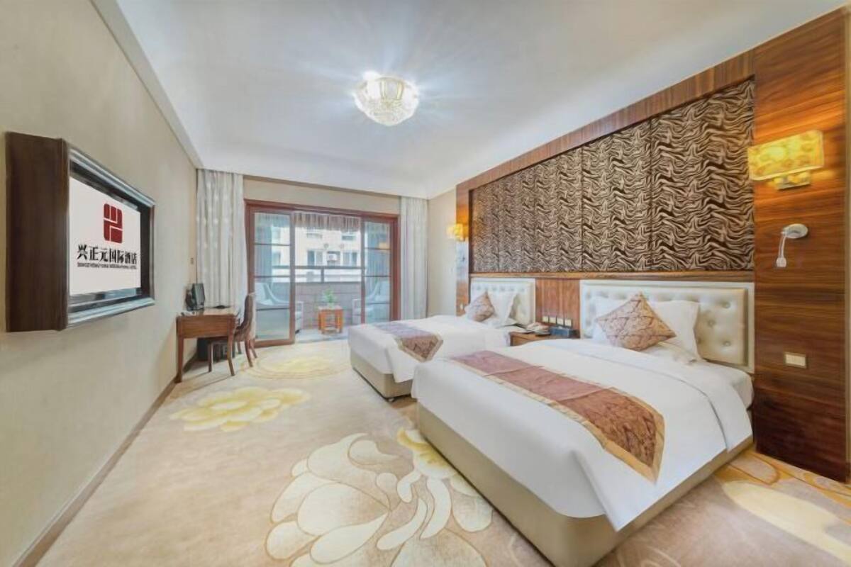 A hotel room with two beds, a desk, a chair, a large window, and a decorative wall panel.