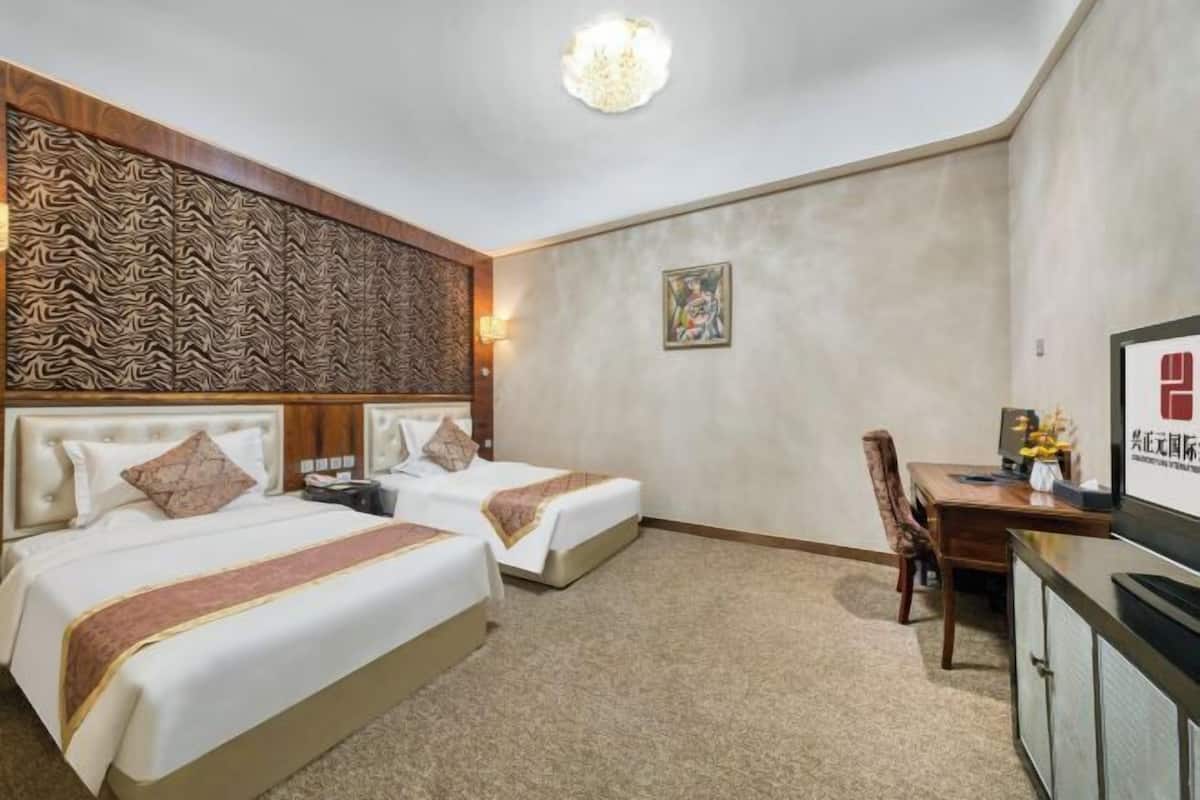 A hotel room with two beds, a desk, a chair, and a television.