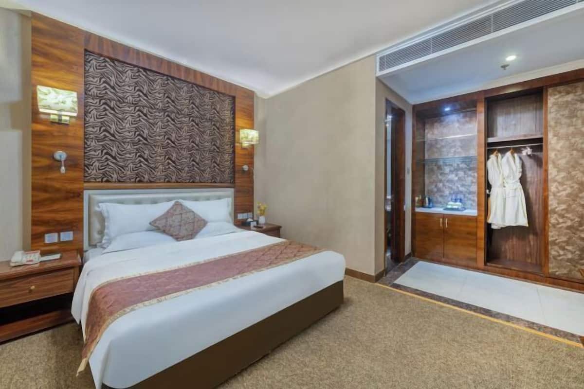 A hotel room with a large bed, a wardrobe, a mirror, and a nightstand.