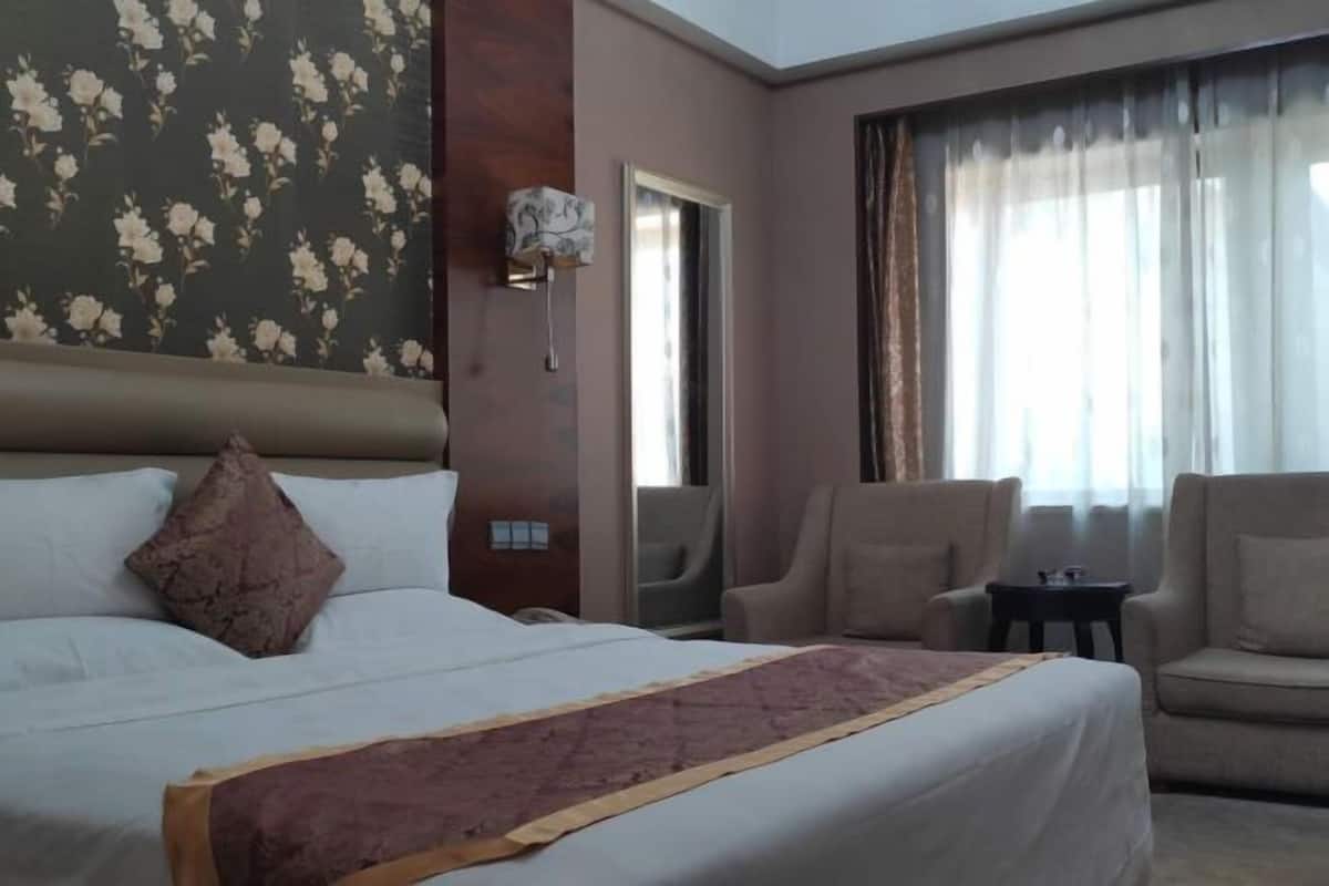 A hotel room with a large bed, a sofa, a small table, and a window with curtains.