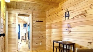 Een houten interieur met een gang die naar een andere kamer leidt, een kleine tafel met een stoel en een lamp aan de muur.