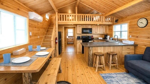 Een houten cabin met een keuken, een eethoek en een trap.