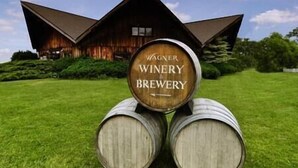 Een houten vat met de tekst 'Wagner Winery & Brewery', geplaatst voor een groot houten gebouw met een schuin dak.