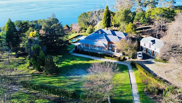 A large house with a swimming pool, surrounded by lush greenery and a view of a lake.