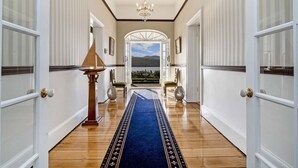 A hallway with a chandelier, a blue carpet, and a view of a mountain through an open door.