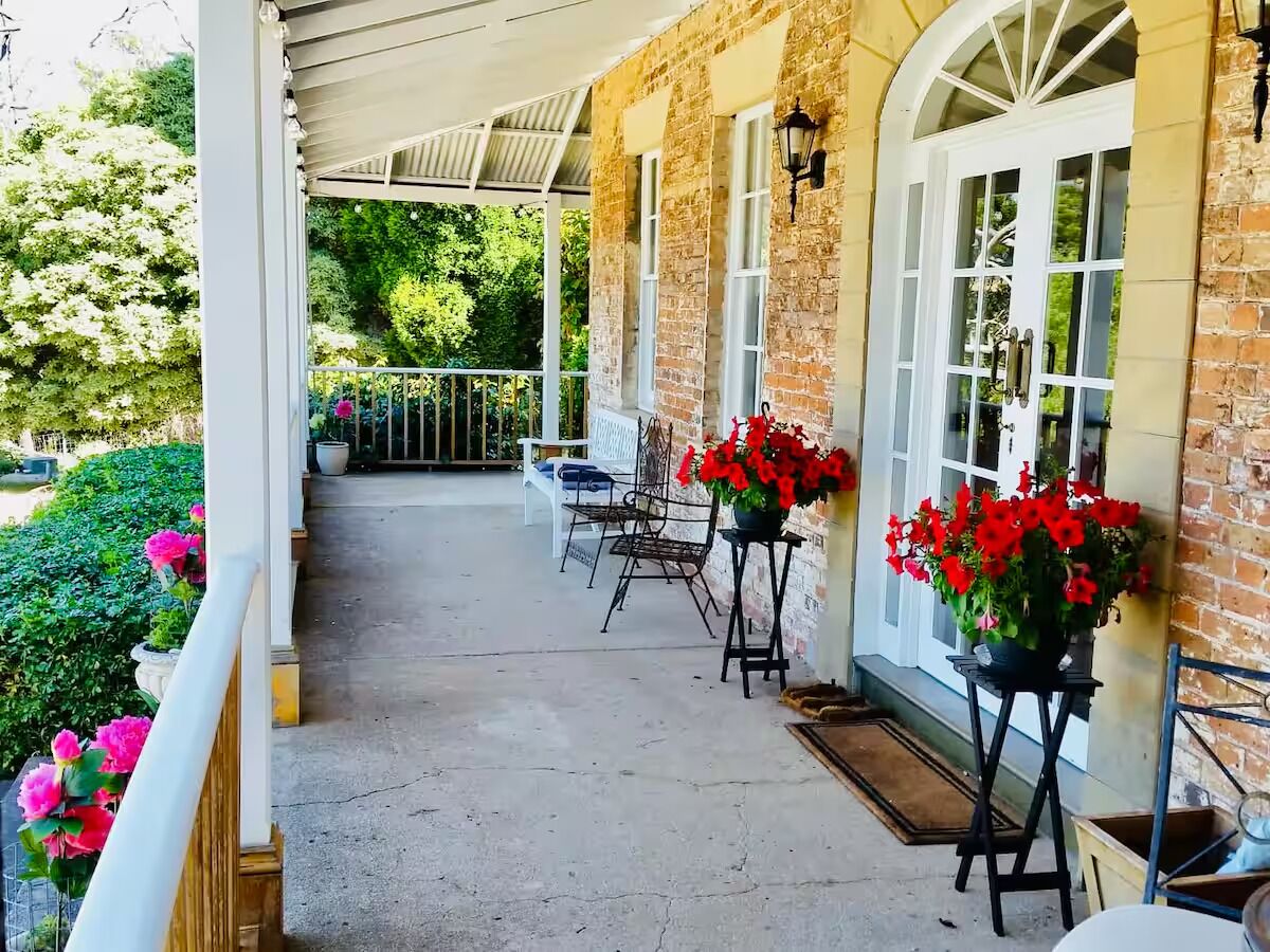 A covered porch with brick walls, white-framed windows, and a bench.