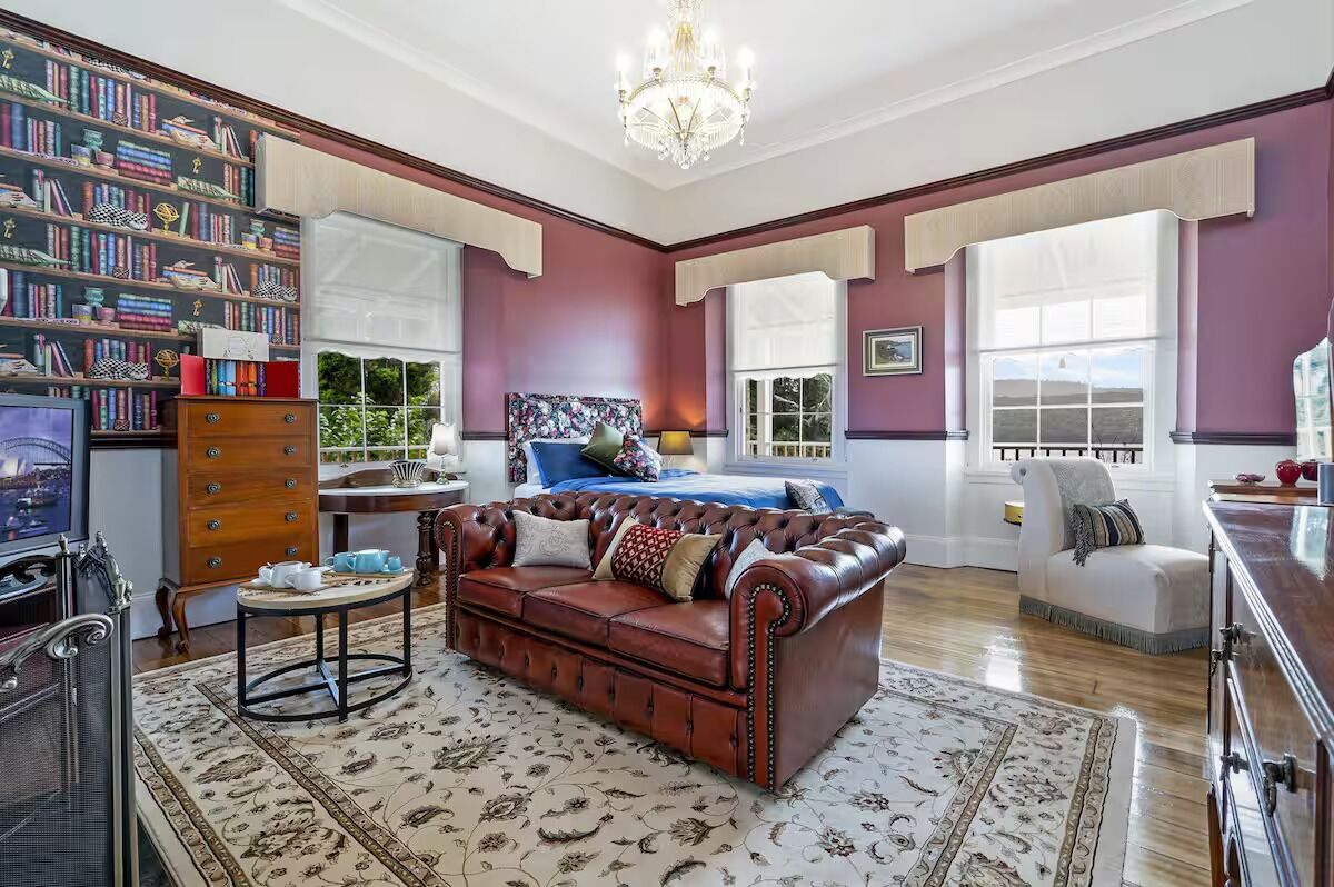 A spacious living room with a large brown leather sofa, a round coffee table, and a bookshelf filled with books.