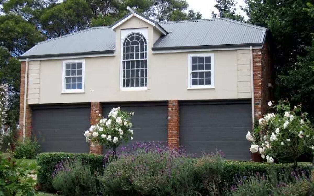 Une maison à deux étages avec un garage, une fenêtre centrale en arc de cercle et une façade en briques.