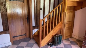 Un escalier en bois avec une rampe, une porte en bois avec une poignée en métal et un sol à carreaux.