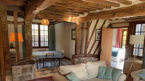 Un intérieur rustique avec des poutres apparentes, un sol à carreaux, un canapé avec des coussins et une table à manger avec des chaises.