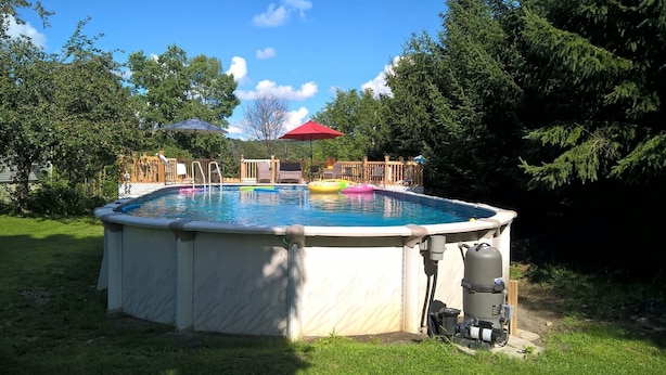 Een bovengronds zwembad met een jacuzzi, omgeven door een houten terras en bomen.