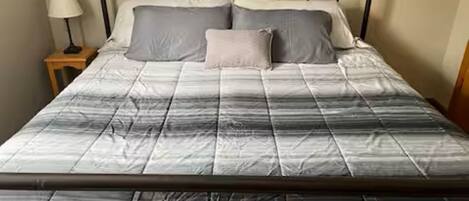 Un lit avec un cadre en métal, une couette rayée de gris et de blanc, et deux oreillers.