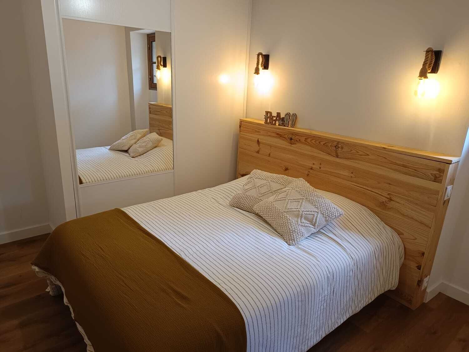 A bedroom with a wooden headboard, a bed with striped bedding, a brown throw blanket, and two wall-mounted light fixtures.