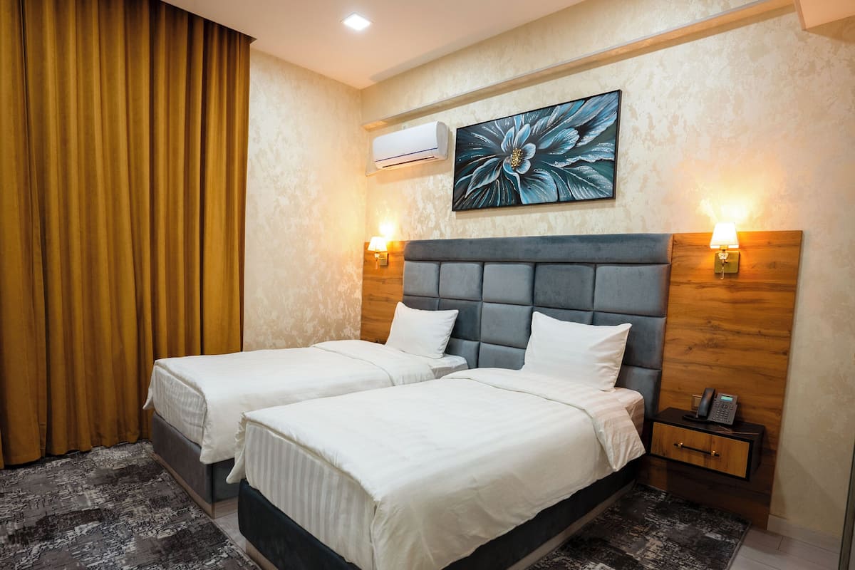 A hotel room with two beds, a large floral artwork on the wall, an air conditioning unit, and a bedside table with a phone.