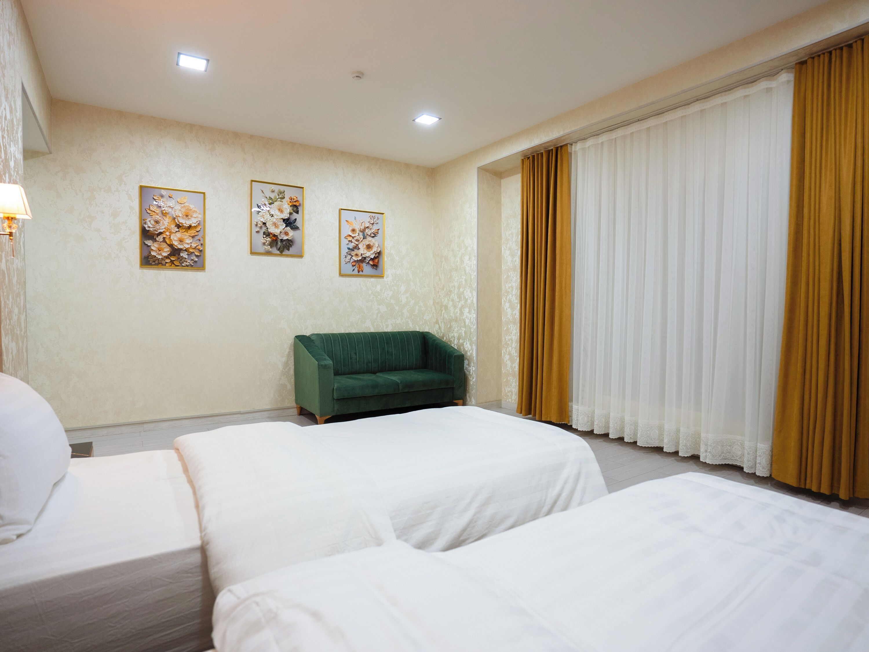 Une chambre d’hôtel avec deux lits, un fauteuil vert et trois tableaux aux motifs floraux accrochés au mur.