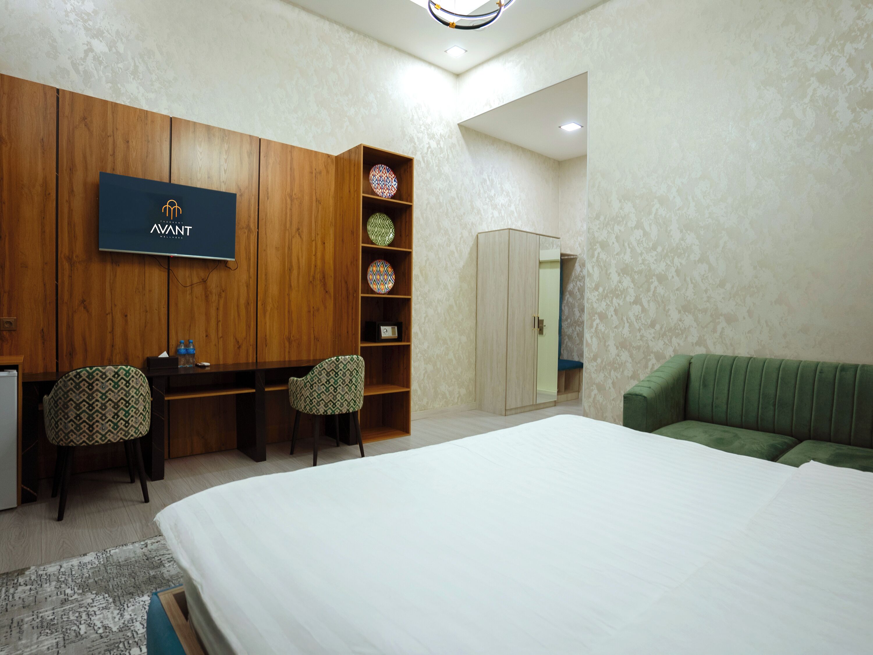 Een hotelkamer met een bed, een bureau met twee stoelen, een kledingkast, een televisie en een groene bank.