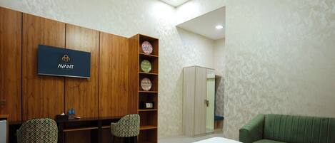 A hotel room with a bed, a desk with two chairs, a wardrobe, a television, and a green sofa.