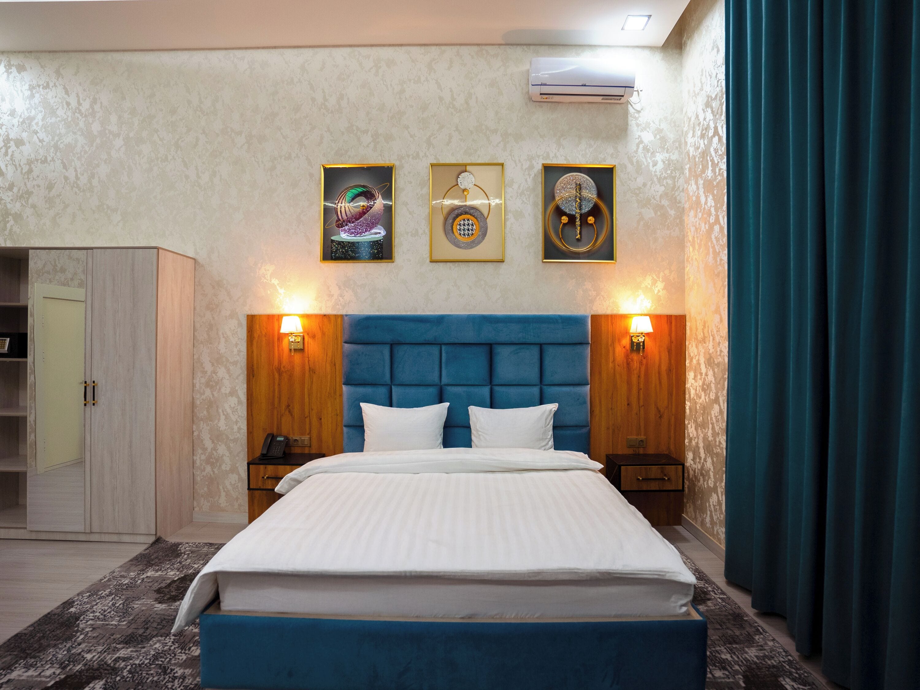 Una camera d'albergo con un letto grande, una testiera in legno, due comodini con lampade, un armadio e tre opere d'arte incorniciate appese al muro.