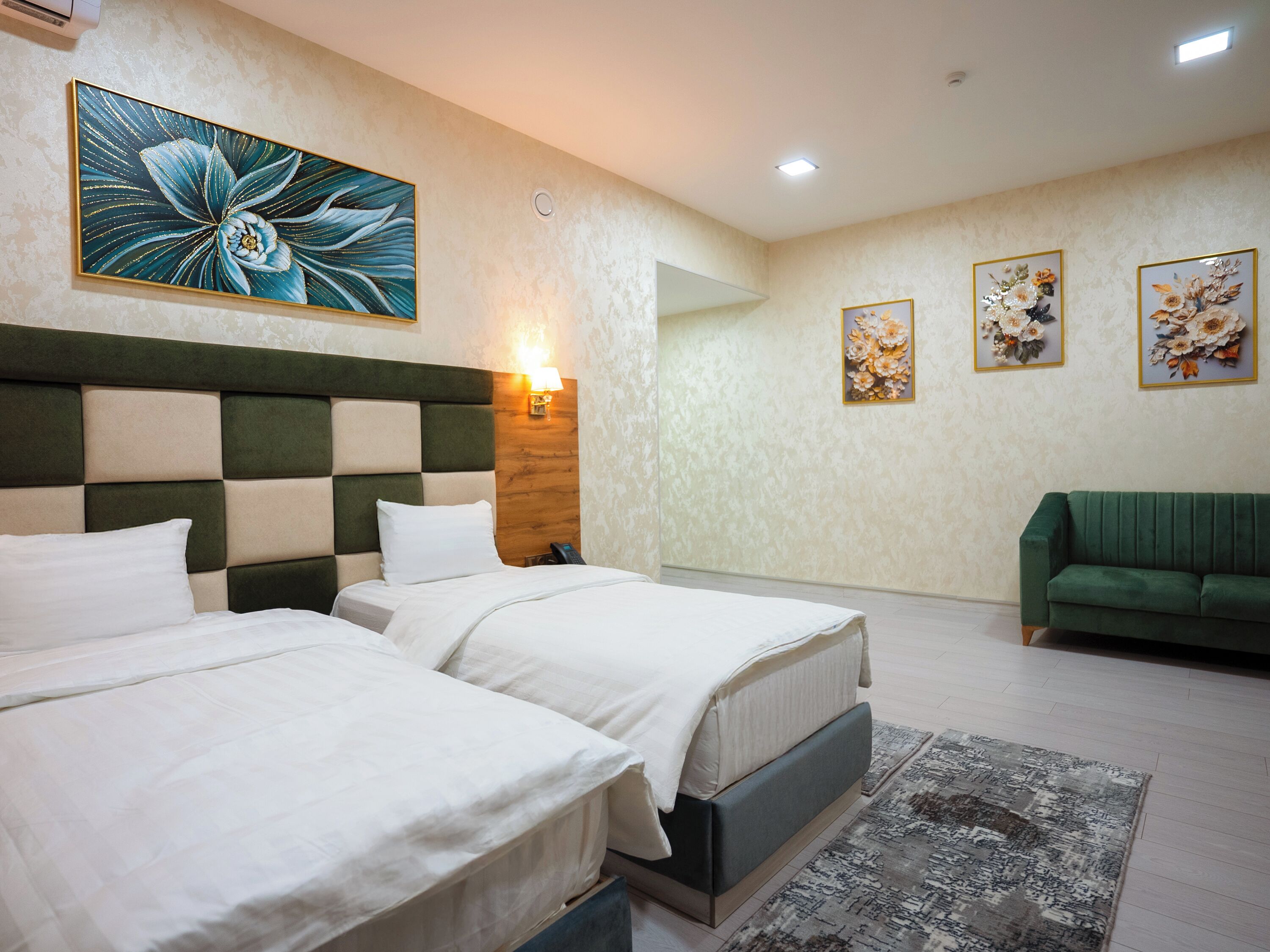 Een hotelkamer met twee bedden, een groene bank en bloemmotieven aan de muur.