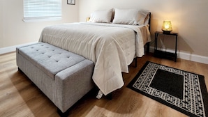 A bedroom with a large bed, a bench, a nightstand with a lamp, a window with blinds, and a ceiling light. - Toria Suites 922 (Lakeland)