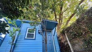 Ein blaues Haus mit einer Haustür, einem kleinen Fenster und einem Baum davor.