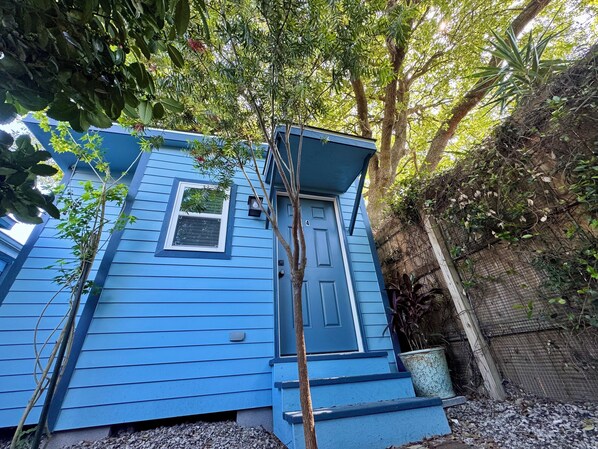 A blue house with a front door, a small window, and a tree in front.