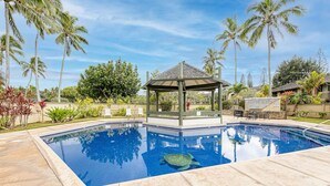 Una piscina con un pabellón, palmeras y un patio con sillas y mesas.