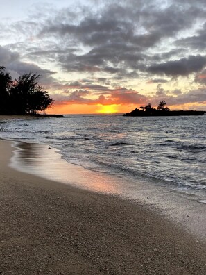 A beach with a sunset, calm waves, and silhouettes of trees. - Charming 1-bedroom condo in 3 min from beach with lots of beach toys (Kahuku)