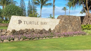 Un cartel de Turtle Bay con un muro de piedra y flores rosas.