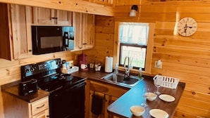 L’intérieur d’une cabane en bois comprend une cuisine équipée d’une cuisinière, d’un four à micro-ondes, d’un évier et de tabourets de bar.