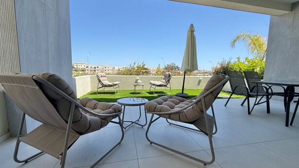 Ein Balkon mit zwei gepolsterten Stühlen, einem kleinen Tisch und einem Esstisch mit Stühlen.