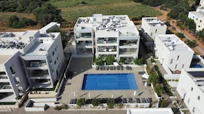 Un immeuble moderne à plusieurs étages, doté d’une piscine sur le toit, d’un espace extérieur aménagé et de panneaux solaires.