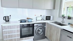 A modern kitchen with a dishwasher, washing machine, microwave, and kettle.