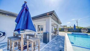 Un espace aménagé au bord de la piscine, avec un coin salon couvert, une piscine et un ciel dégagé.